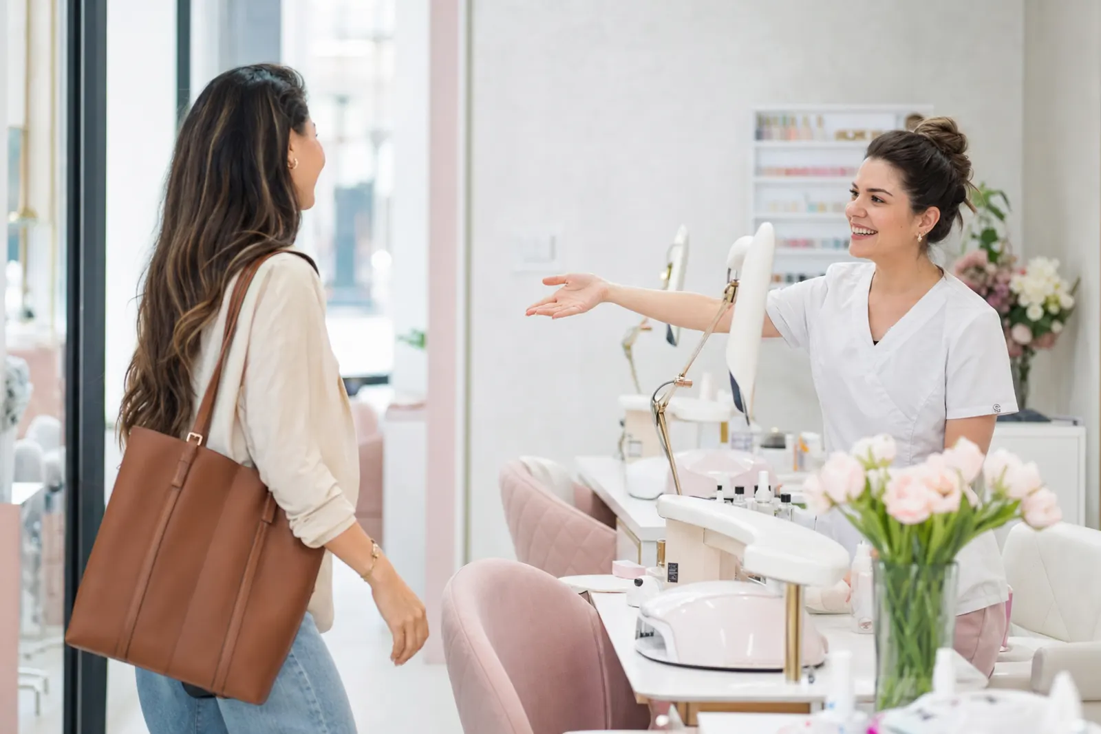 Manicurista saludando con una sonrisa a una clienta habitual que entra al Nails Spa